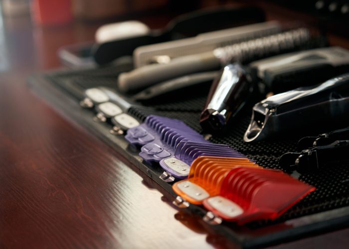 Selective focus of working tools of barber master in barbershop. Hair salon wooden table with trimmer machine, brushes and colorful plastic grooming tools indoors. Concept of haircare, beauty.